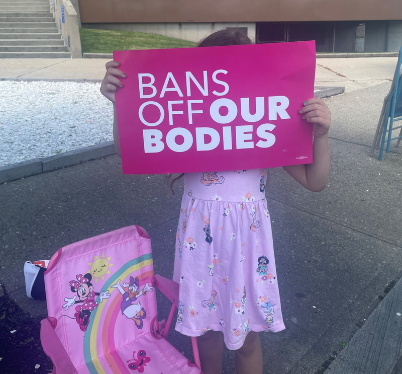 Child at Reproductive Justice rally hold signs saying, “Bans off our bodies.
