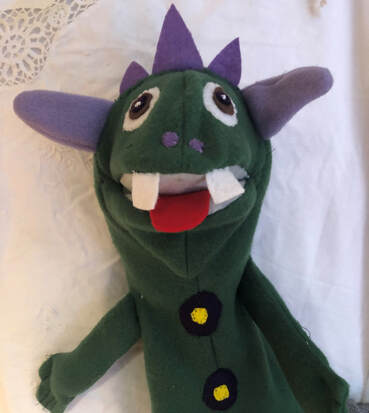 Photo of decorated puppet with purple horns, red tongue, two front  teeth, green clothing and black and gold buttons