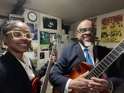 Photo of Fred Woodard holding a guitar and daughter Deniece holidng a bass guitar with bulletin boards in the background