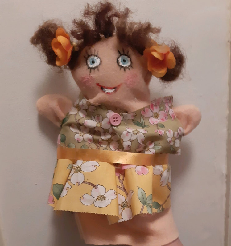 Photo of puppet dressed up in a flowered top and skirt wearing orange bows in her pigtails