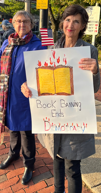 2 BCCR members stand out at 9/26/23 book banning rally. One holds a sign showing books on fire, with the text, "Book banning ends democracy."